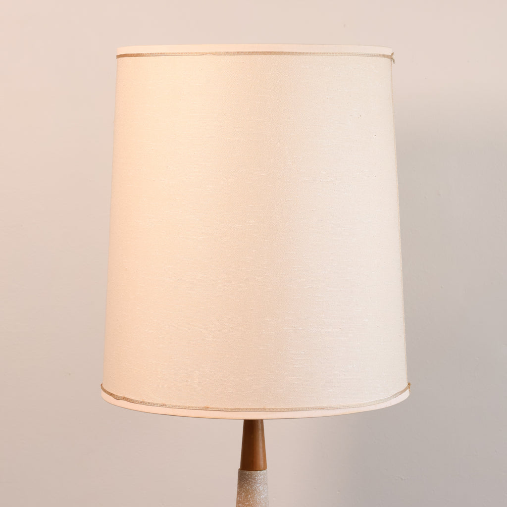 A classic drum lampshade in a warm cream or off-white linen fabric, shown on a matching table lamp against a neutral light beige background.