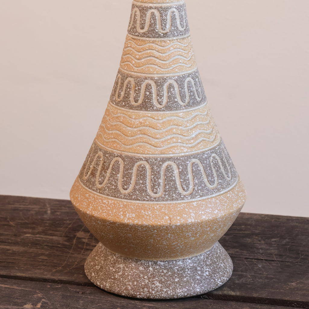 A decorative ceramic lamp base with a conical neck and flared pedestal foot, featuring a speckled beige and gray glaze with wavy geometric bands.