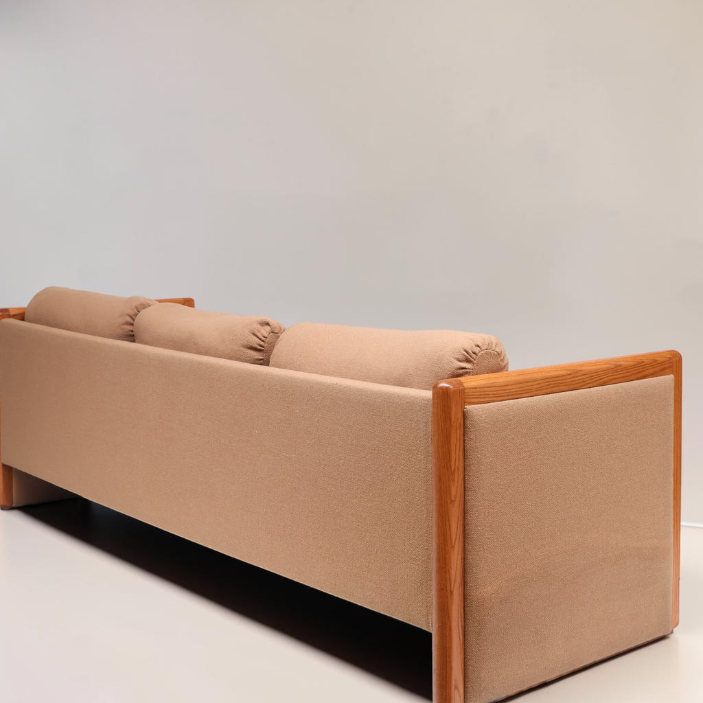 Image features the back of a brown mid-century modern wool sofa with a wooden frame against a white background.