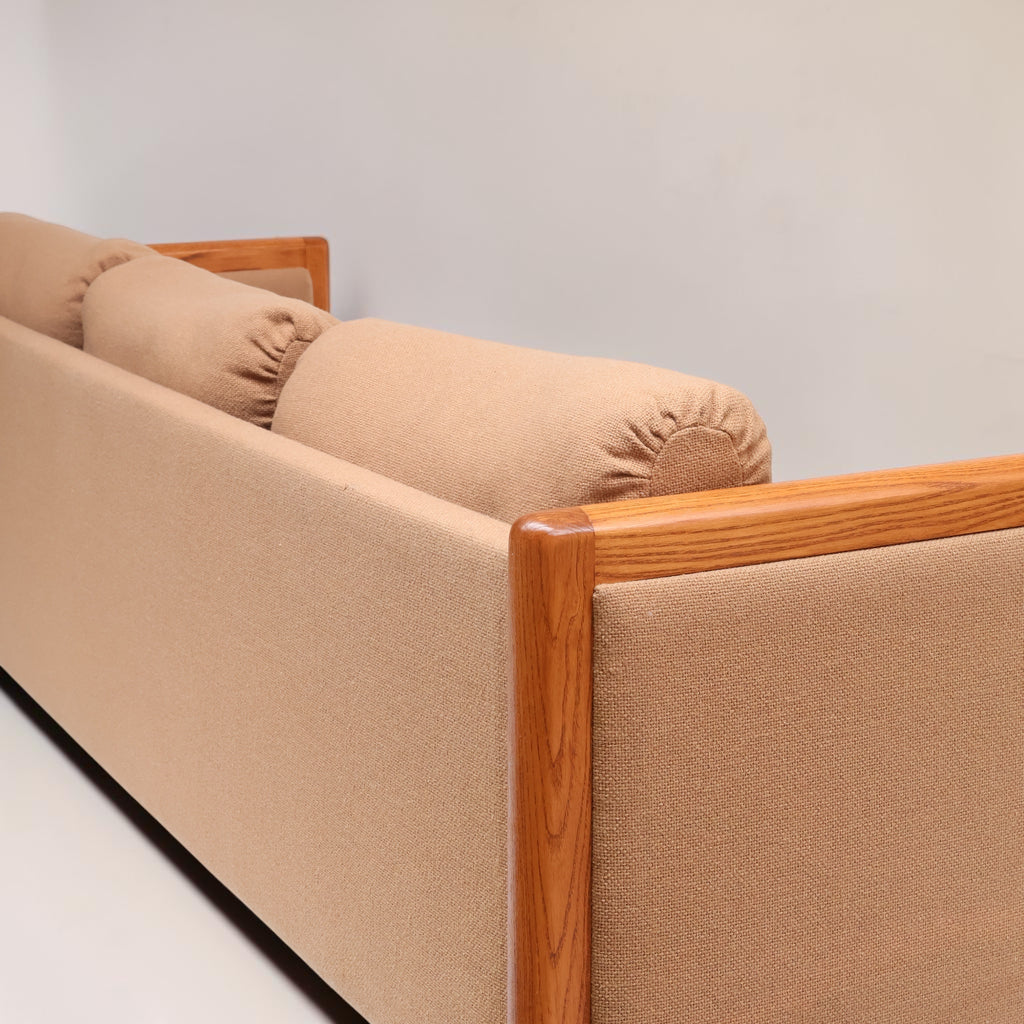 Image features a corner of a brown mid-century modern wool sofa with a wooden frame against a white background.