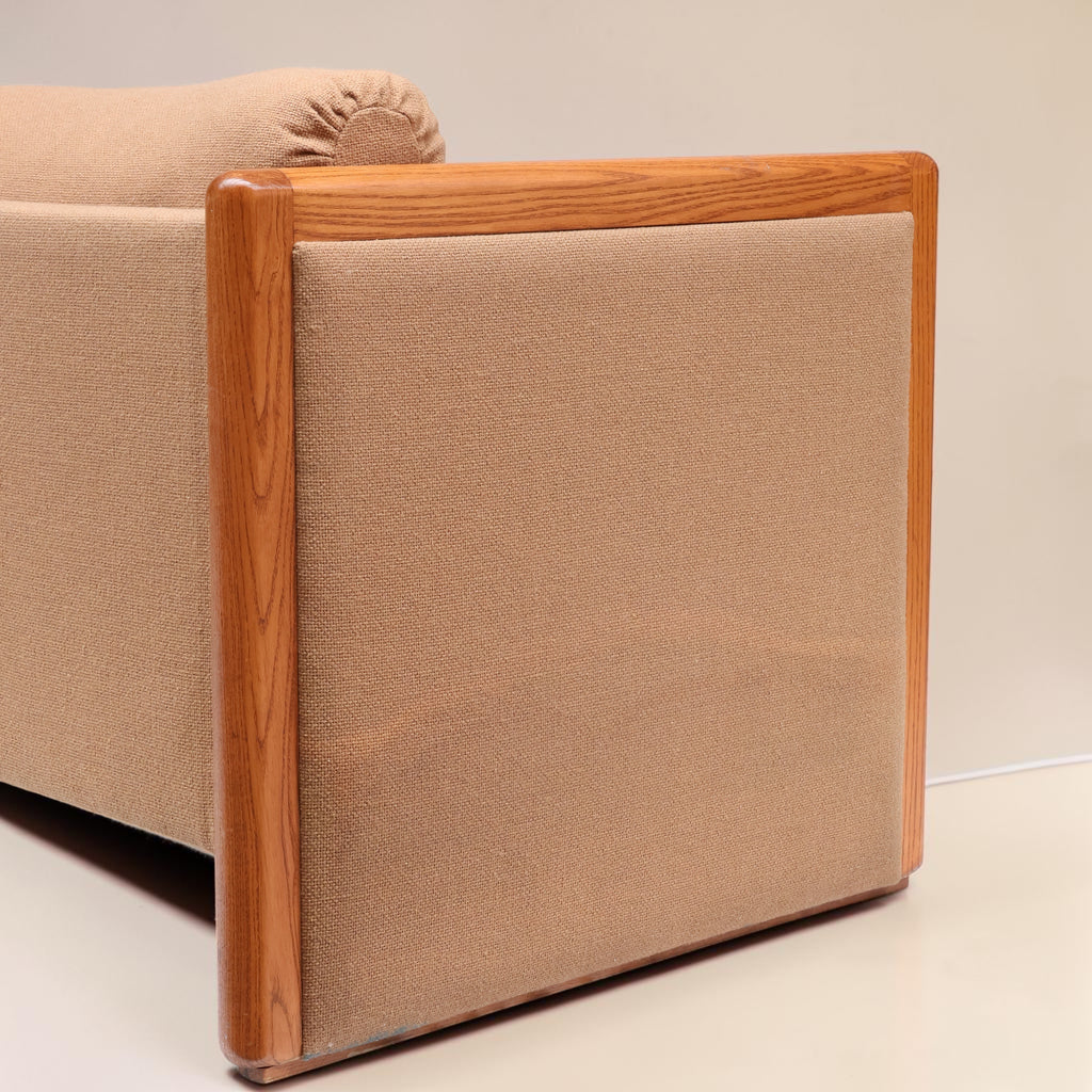Image features a close up of the side of a brown mid-century modern wool sofa with a wooden frame against a white background.