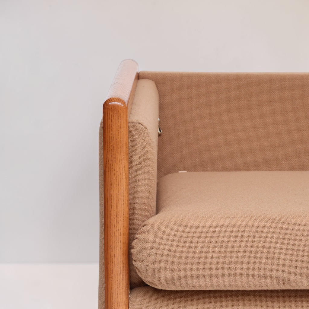 Image features a close up of the arm of a brown mid-century modern wool sofa with a wooden frame against a white background.