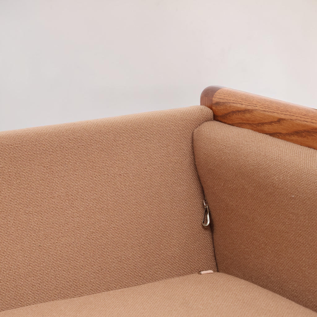Image features the corner of a brown mid-century modern wool sofa with a wooden frame against a white background.