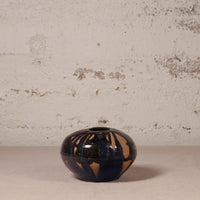 Small ceramic vase with blue and brown glaze on a textured surface