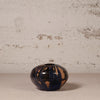 Small ceramic vase with blue and brown glaze on a textured surface