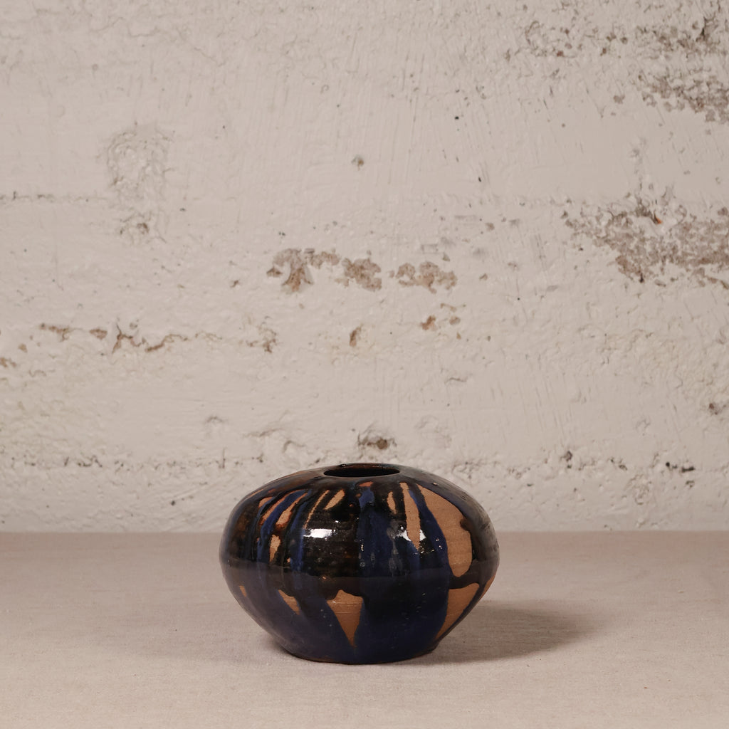 Small ceramic vase with blue and brown glaze on a textured surface