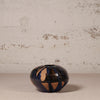 Small ceramic vase with black and gold design on a textured surface