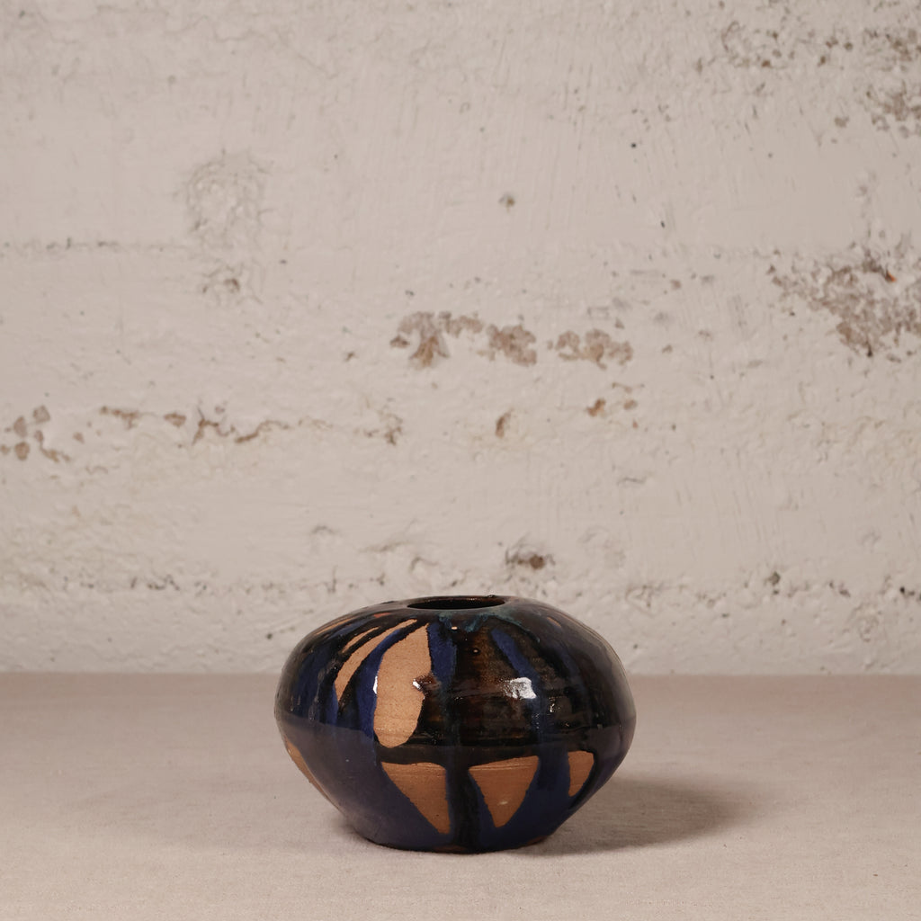 Small ceramic vase with black and gold design on a textured surface