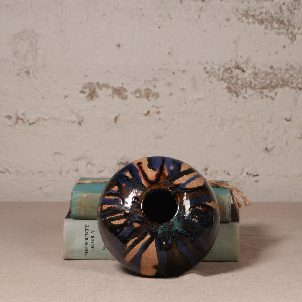 Decorative ceramic vase with a unique design on top of books against a textured wall.