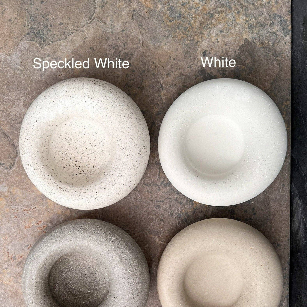 Four round concrete-style bowls or candle holders shown in two color options: Speckled White, White, Speckled Gray, and Cement Gray, arranged on a textured stone surface with text labels.