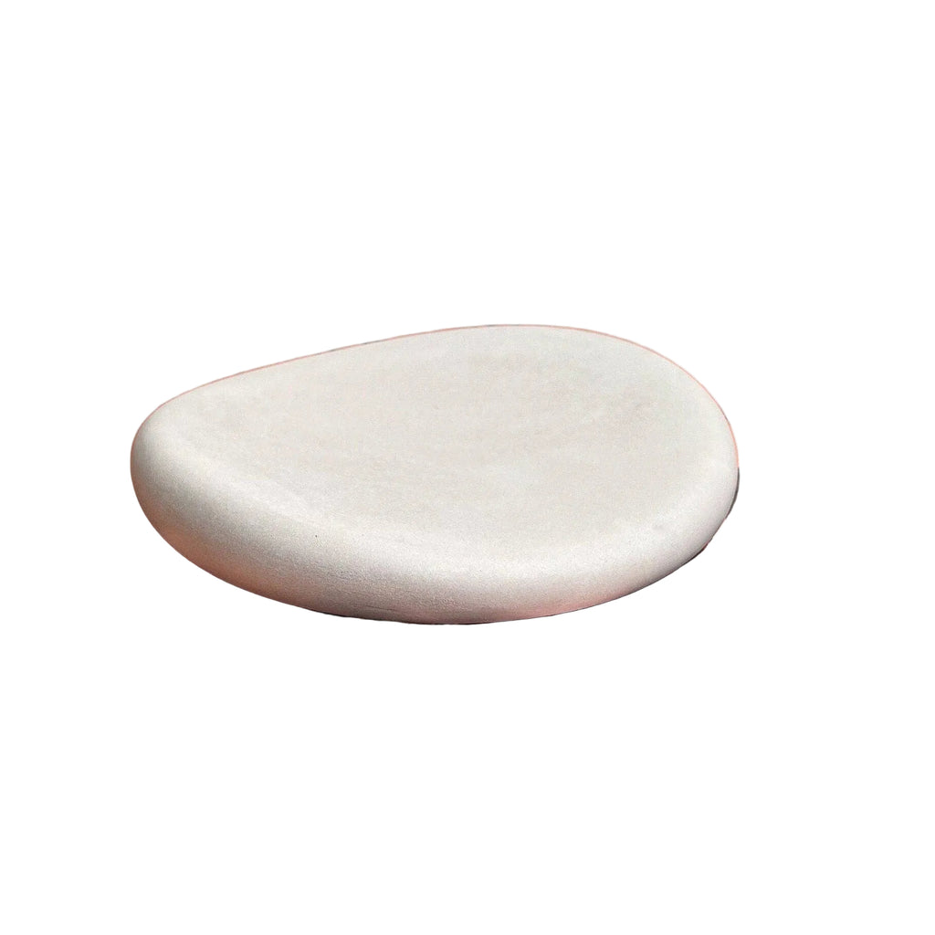 A round, matte white ceramic or stone dish resting on top of a peach-colored book with a floral cover.