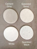 Four circular stone or concrete swatches arranged in a 2x2 grid on a textured taupe background, labeled Cement Gray, Speckled Sand, White, and Speckled Black.