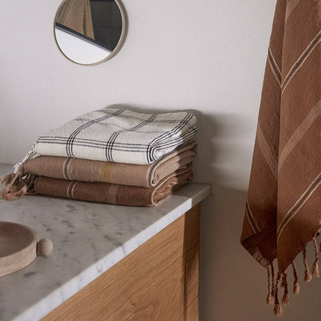 Stack of folded towels on a marble countertop with a round mirror and hanging towel in the background.
