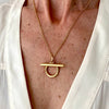 Gold necklace with a unique pendant on a person wearing a white shirt.