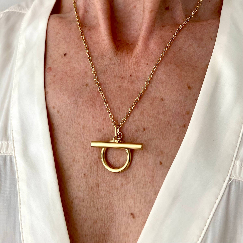 Gold necklace with a unique pendant on a person wearing a white shirt.