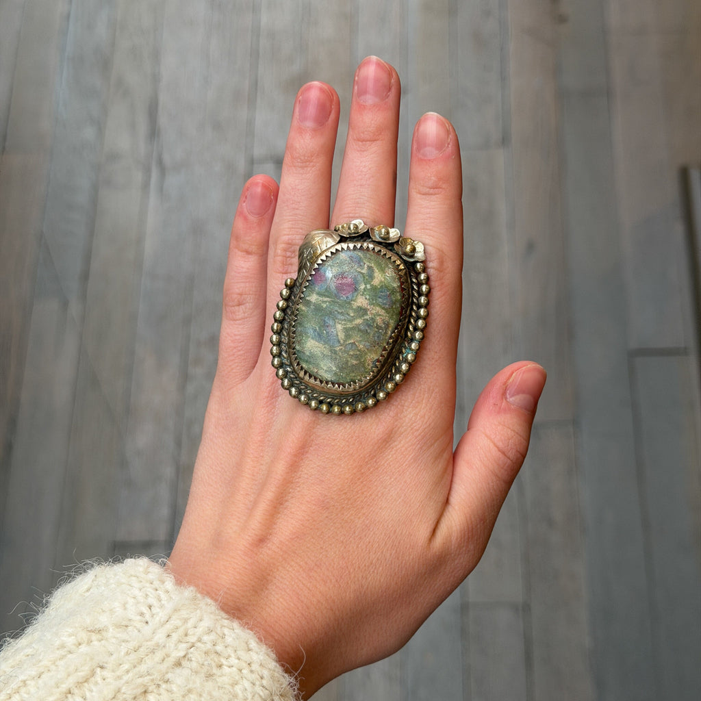 Hand wearing a large, ornate ring with a stone on a neutral background