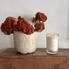 Candle and dried flowers on a wooden surface with a neutral background