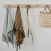 Three scarves and a basket hanging on a wooden rack against a white wall.