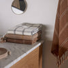 Stack of folded towels on a marble countertop with a round mirror and hanging towel in the background.