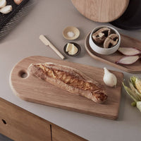 Wooden cutting board with bread on a kitchen counter with various items.