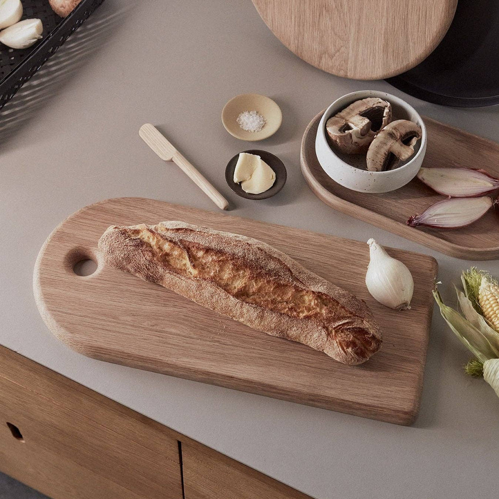 Wooden cutting board with bread on a kitchen counter with various items.