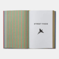 An open book or magazine on a light gray background. The left page has vertical stripes in green, pink, and blue, while the right page is white with the text 'STREET FOOD' and a black bird silhouette.