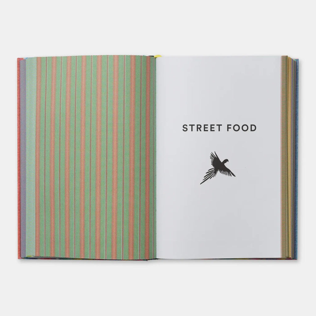 An open book or magazine on a light gray background. The left page has vertical stripes in green, pink, and blue, while the right page is white with the text 'STREET FOOD' and a black bird silhouette.