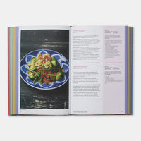 An open printed cookbook or recipe book spread, showing a plated green salad on the left page and recipe text on the right page, photographed against a light gray background.