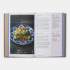 An open printed cookbook or recipe book spread, showing a plated green salad on the left page and recipe text on the right page, photographed against a light gray background.