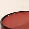 Close-up of a translucent red glass bowl or cup with a glossy black rim against a plain light background.