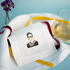 Embroidered napkin with a portrait on a table setting with a glass of water and flowers.