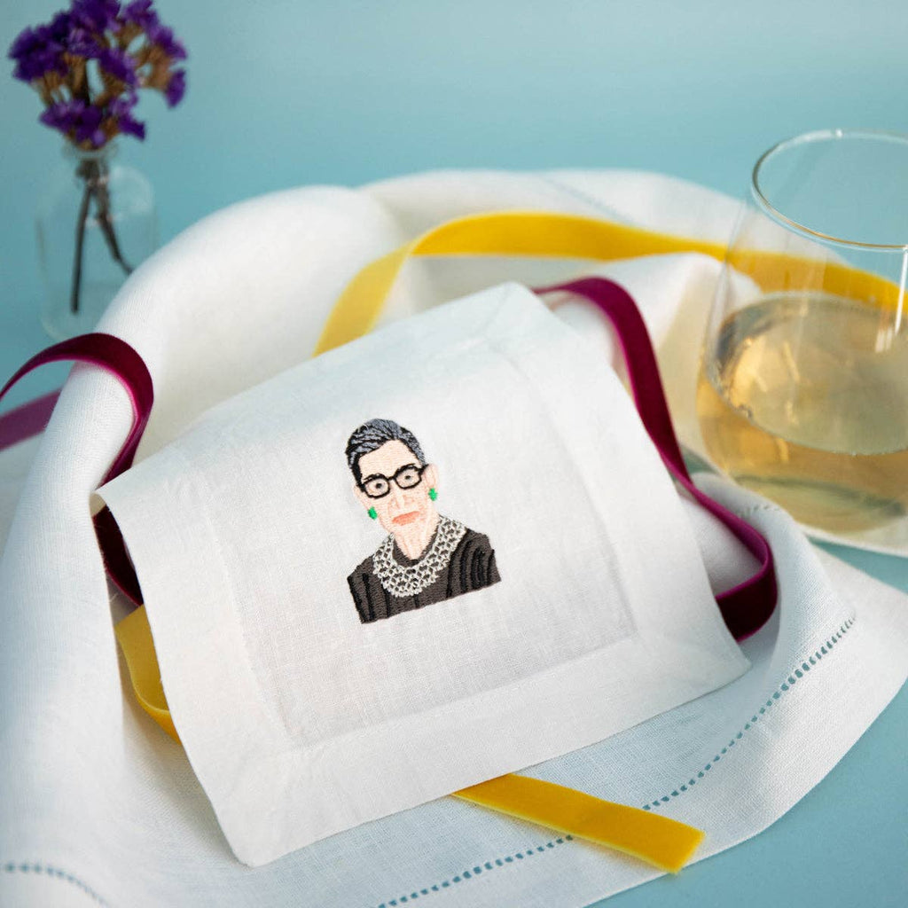 Embroidered napkin with a portrait on a table setting with a glass of water and flowers.