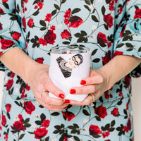 Person holding a white tumbler with a design, wearing a floral dress.