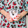 Person holding a white tumbler with a design, wearing a floral dress.