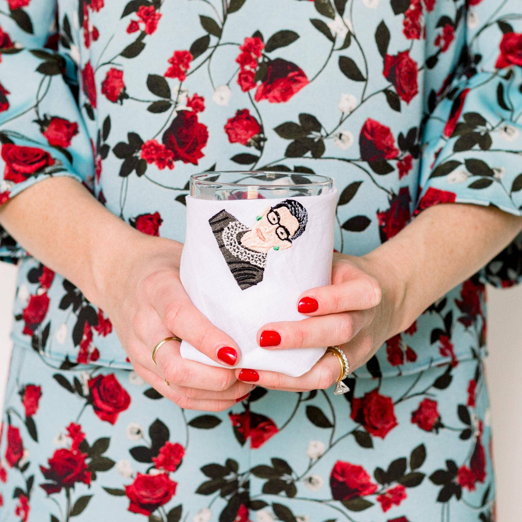 Person holding a white tumbler with a design, wearing a floral dress.