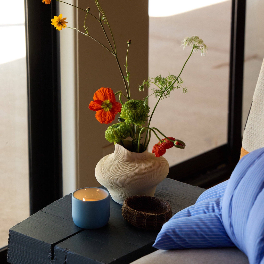 Vase with flowers on a table next to a candle and blue fabric