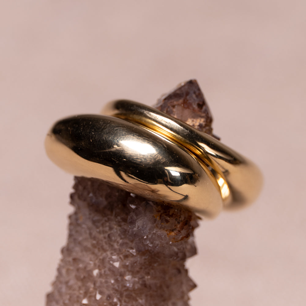 A pair of polished gold rings displayed on a textured crystal against a soft beige background.