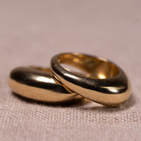 Two overlapping matte gold rings resting on a textured beige fabric surface.