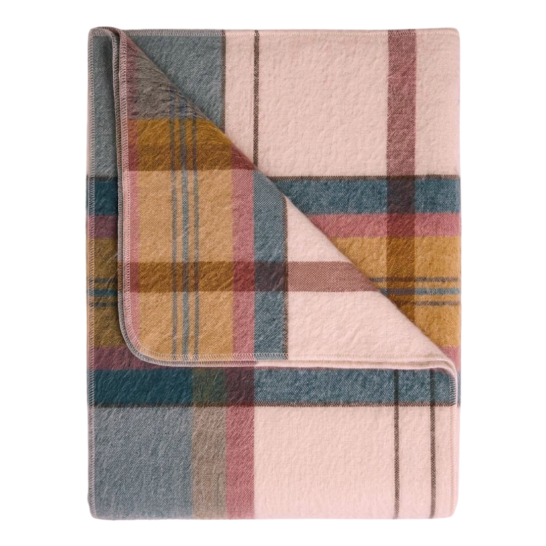 A folded plaid blanket with a soft, fuzzy texture, featuring a color palette of dusty pink, slate blue, mustard yellow, and muted red on a white background.