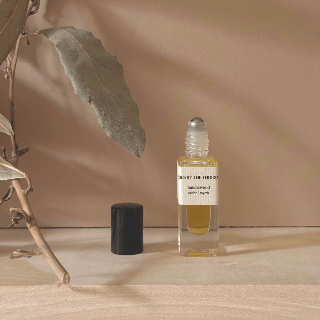 Small glass rollerball bottle with sandalwood essential oil on a wooden surface with a leaf and branch.