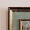 Close-up of a framed artwork with a brown frame on a beige wall.