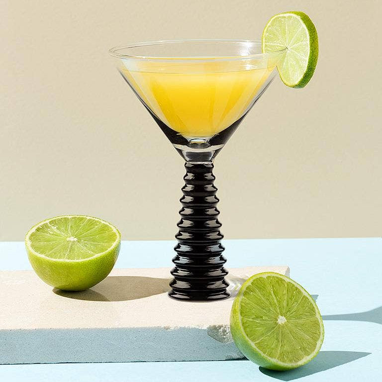 Martini glass with yellow liquid and lime garnish on a light background