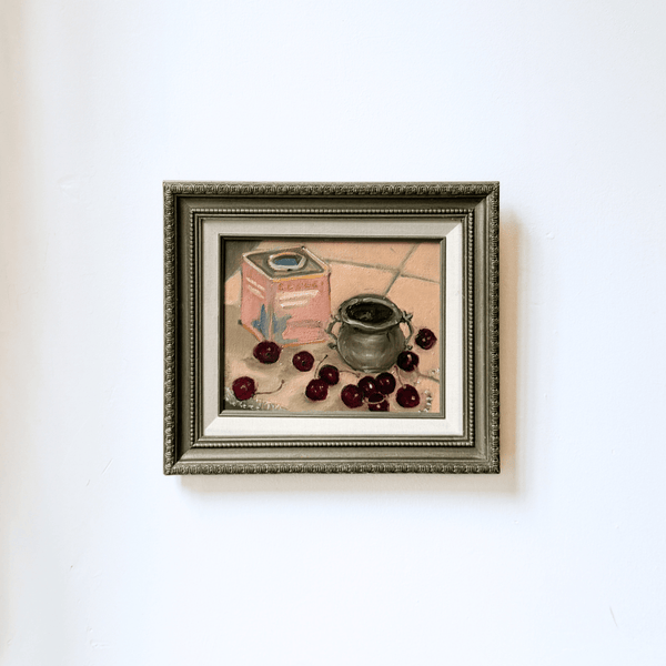 Framed still life painting with cherries and a pot on a white wall