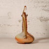 A hand-blown glass pitcher with a bulbous base, a tall ribbed neck, and a curved spout, featuring a marbled color palette of orange, brown, beige, and white, set against a textured off-white wall.