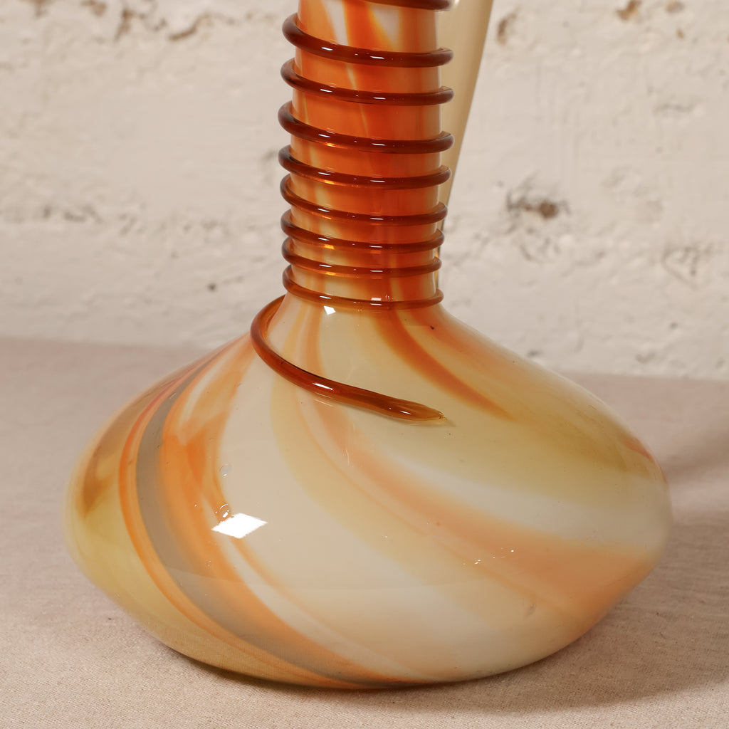A decorative glass vase with a rounded bulbous base, featuring marbled swirls of cream, orange, and brown, with a ribbed neck wrapped in a dark amber-brown spiral.