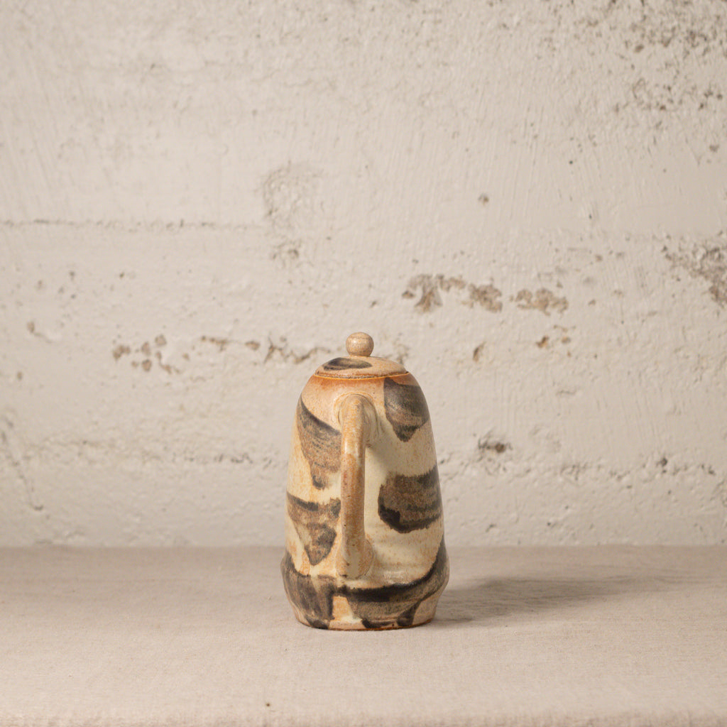 Ceramic pitcher with brown and beige patterns on a textured surface and background