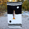 Black and white blanket with colorful design on a sandy beach