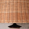 Close-up of a woven natural rattan or wicker lampshade with a dark glossy base visible at the bottom.