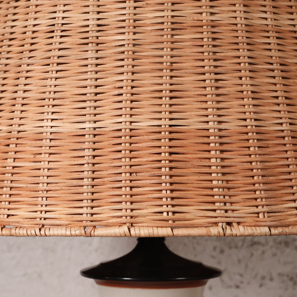 Close-up of a woven natural rattan or wicker lampshade with a dark glossy base visible at the bottom.
