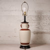 A vintage-style ceramic table lamp with a cream-colored body, brown bands, and a black base, featuring a wire shade and a visible light bulb.
